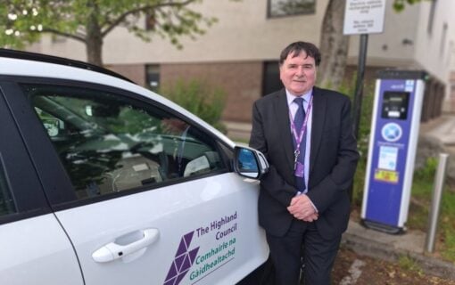 A man stands next to a white car with the highland council logo